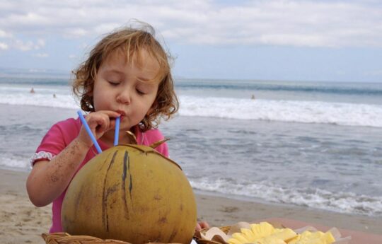 Child having a coconut on the beach in bali