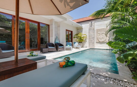 View of swimming pool with two days beds in foreground on sunny day and villa exterior