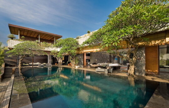 Vierw of swimming pool during day with 2 level Bali villa exterior in background