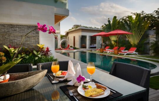 view of swimming pool with breakfast on table in foreground early morning