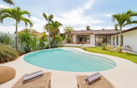 Pool area with day beds of Villa Panas Sekali with palm tres and villa exterior in background